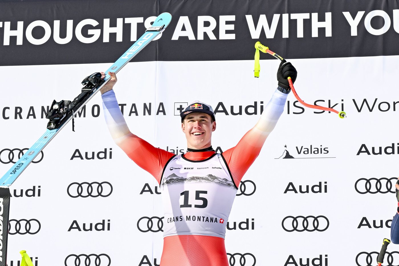 Uśmiechnięty Franjo von Allmen z uniesionymi rękami i nartą na podium w Crans Montana